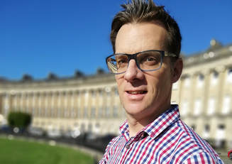 Photo of Simon Cox, director. Man smiling, glasses on